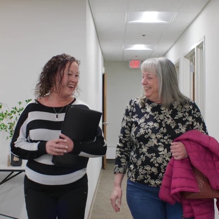 Two women walking and smiling together in a Croghan Bank office hallway