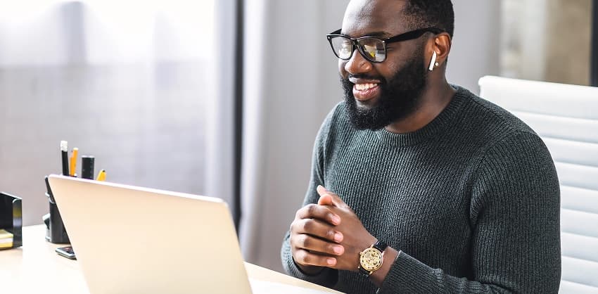 Smiling man in glasses working on a laptop in a modern office setting