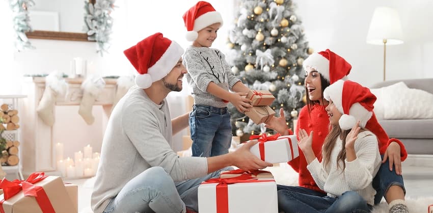 Family in Santa hats exchanging Christmas gifts near a decorated tree