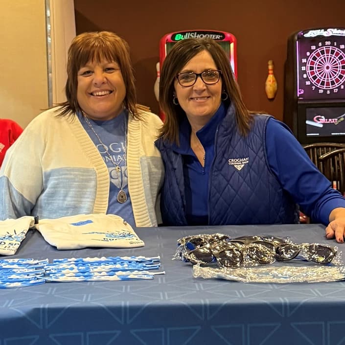 Two Croghan Colonial Bank employees smiling at a promotional event table with branded merchandise