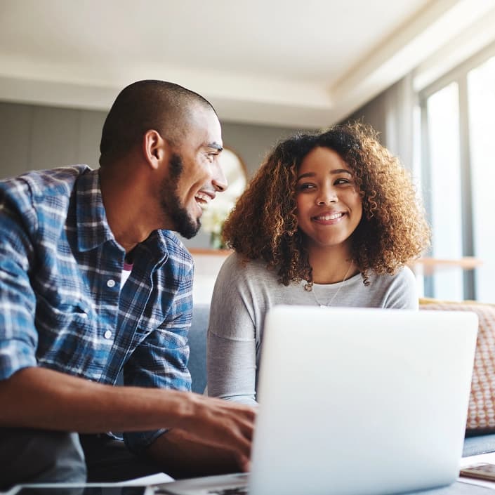 A happy couple browsing online banking options together on a laptop at home.