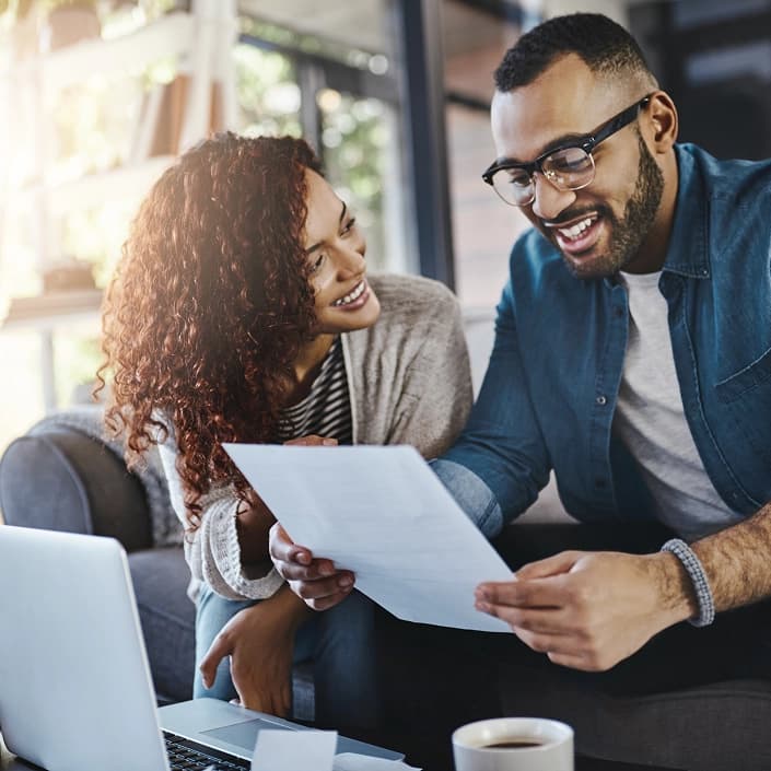 A smiling couple reviewing financial planning documents together at home with a laptop.