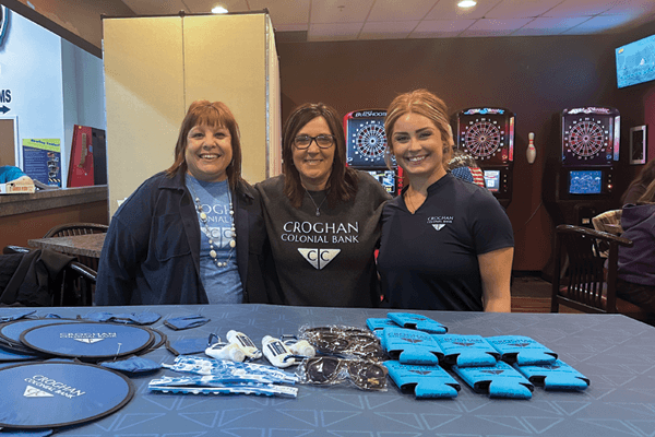 Three Croghan Colonial Bank employees smiling at a promotional table with branded giveaways