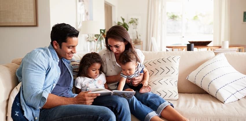 Family relaxing on a couch reading a book together in a bright living room