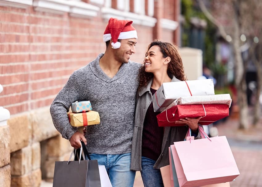 Smiling couple carrying Christmas gifts and shopping bags during holiday shopping