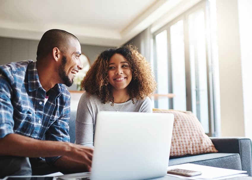 Smiling couple using a laptop together at home for online banking