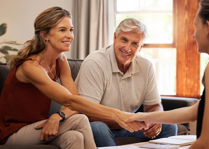 Couple smiling and shaking hands with a financial advisor during a mortgage loan or wealth management consultation