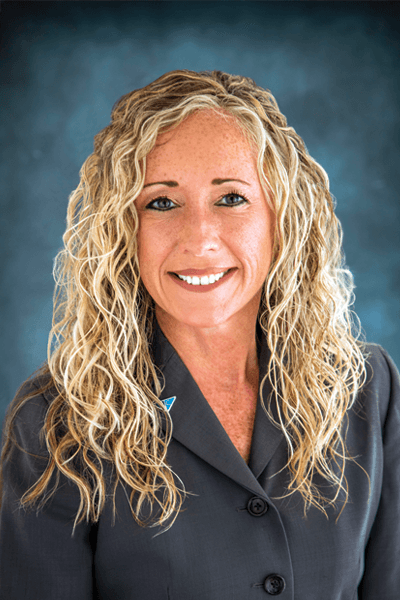 Smiling Croghan Bank employee with long curly blonde hair wearing a gray blazer with a blue lapel pin