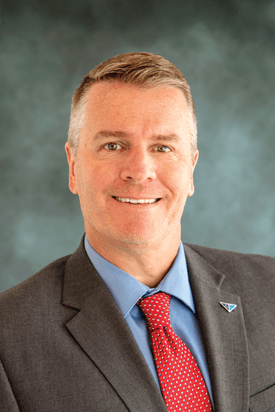 Smiling man with gray hair in a gray suit and red tie with a Croghan Bank pin