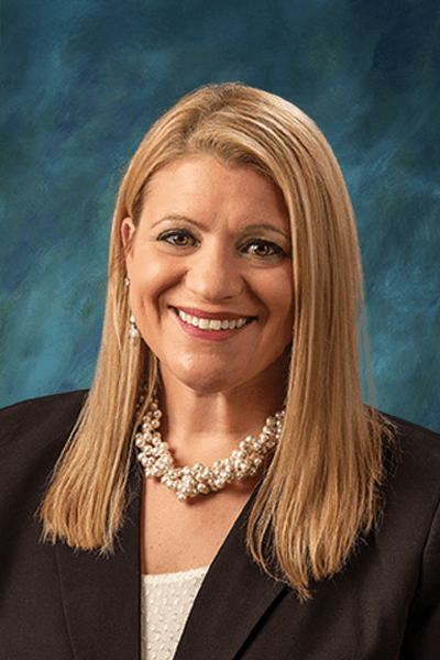 Smiling woman with blonde hair wearing a pearl necklace and dark blazer