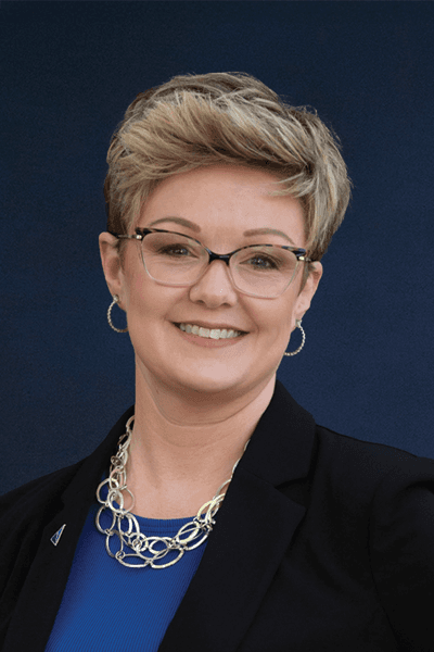 Smiling Croghan Bank employee with short blonde hair, glasses, and a chain necklace wearing a black blazer