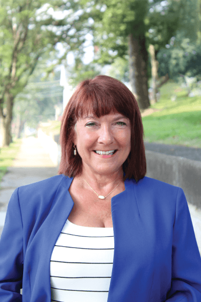 Smiling woman with red hair wearing a blue blazer and striped top outdoors