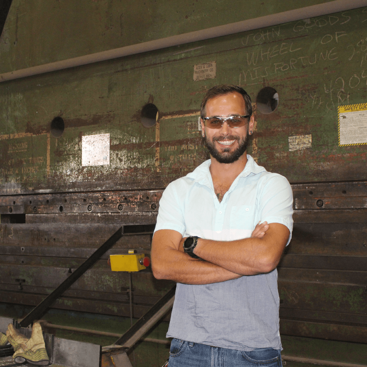 Smiling man with sunglasses and crossed arms standing in front of industrial equipment