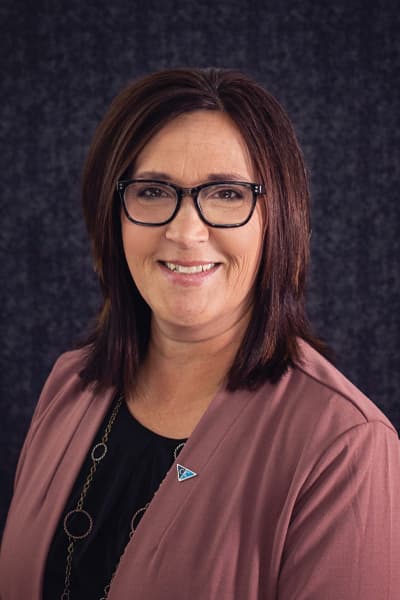 Smiling Croghan Bank female staff member with dark hair and glasses wearing a mauve blazer