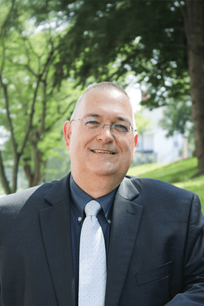 Smiling Croghan Bank professional wearing glasses and a dark suit with a light tie outdoors