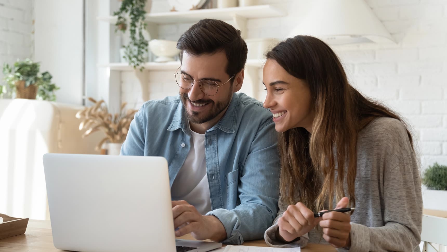 Smiling couple looking at laptop together, reviewing online banking or mortgage loan options at home