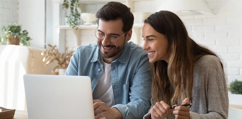 Happy couple browsing online banking options together on a laptop at home