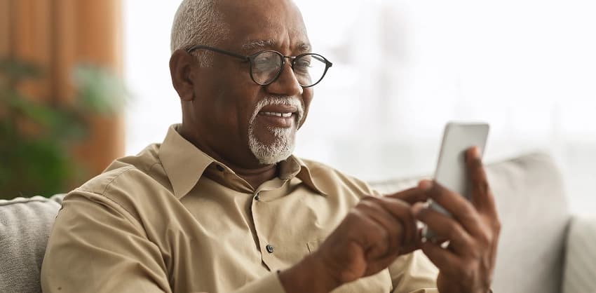 Smiling man with glasses using a smartphone, possibly accessing mobile banking services