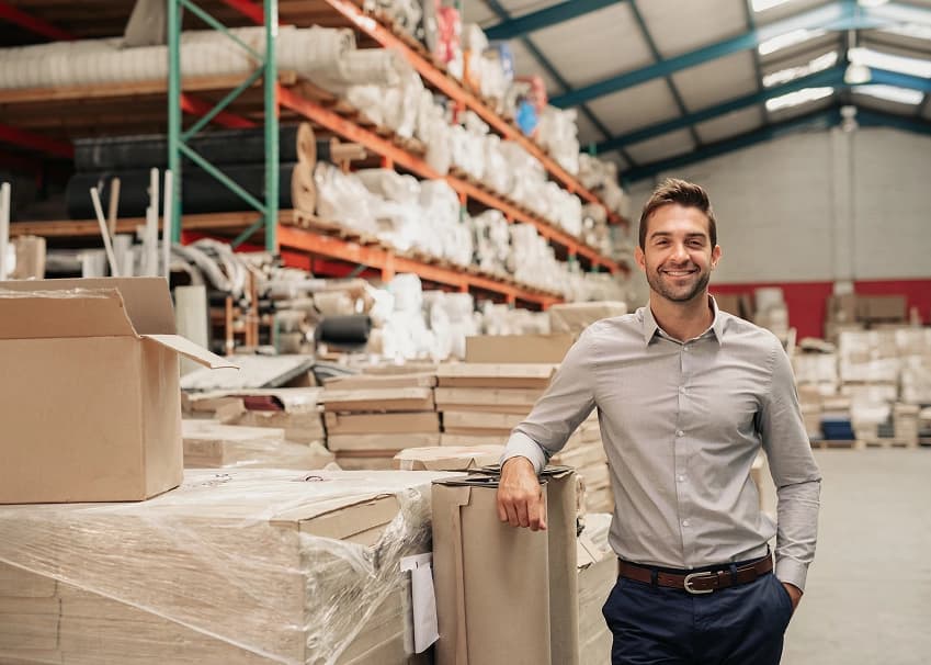 Smiling business owner leaning on stacked boxes in a warehouse
