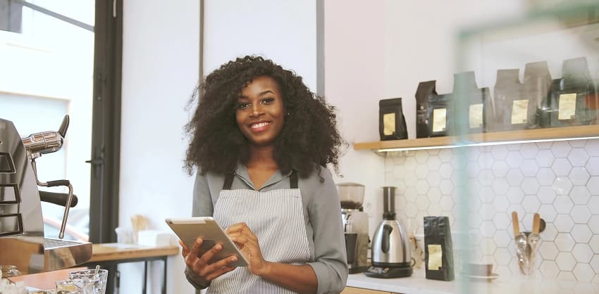 Smiling small business owner holding a tablet in her coffee shop