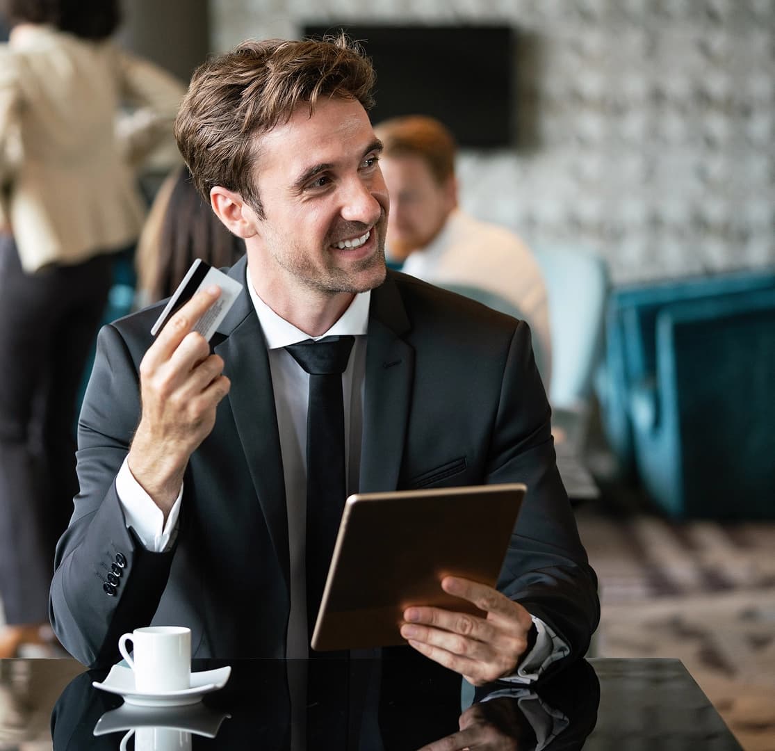 Businessman in a suit holding a credit card and tablet while sitting at a table