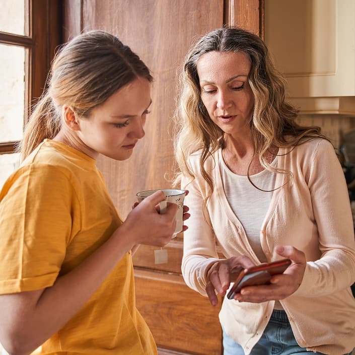 Mother and daughter reviewing information on a smartphone together in a kitchen