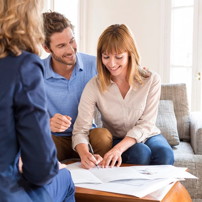 Couple smiling and signing mortgage loan documents with a financial advisor at home