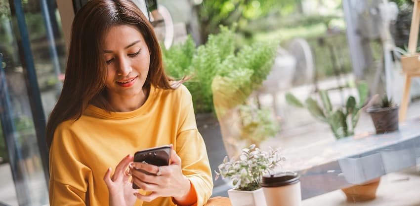 Young woman in a yellow sweater using a smartphone at a café near a window