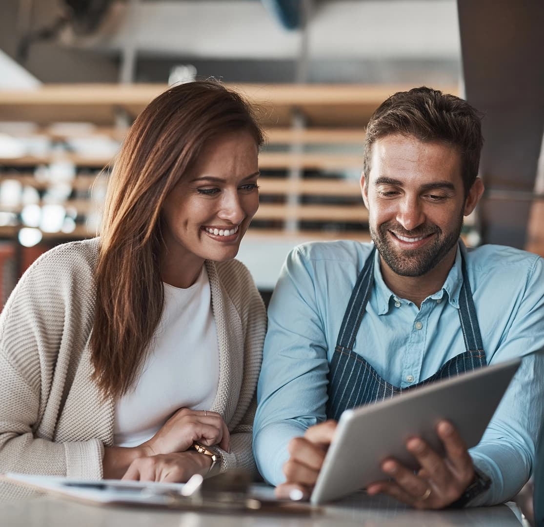 Two small business owners smiling while reviewing information on a tablet together