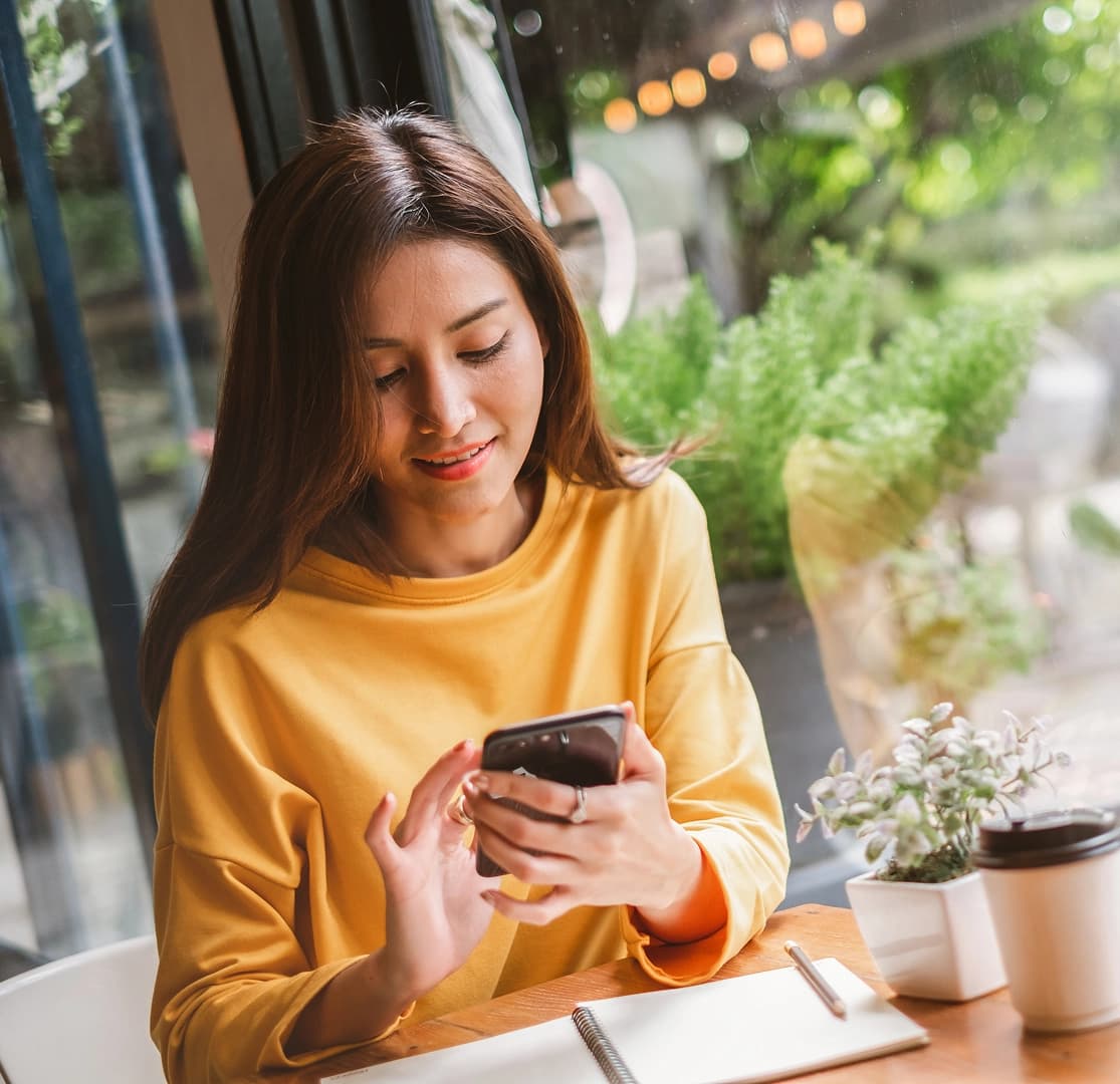 Woman in yellow sweater using smartphone for online banking at a café table