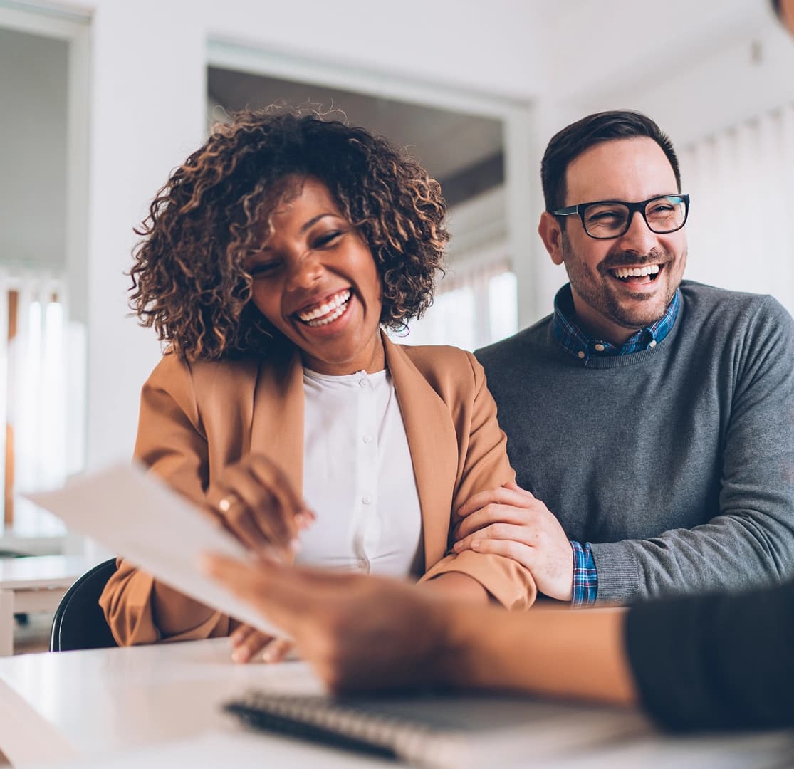Couple laughing while reviewing mortgage loan or financial planning documents with an advisor