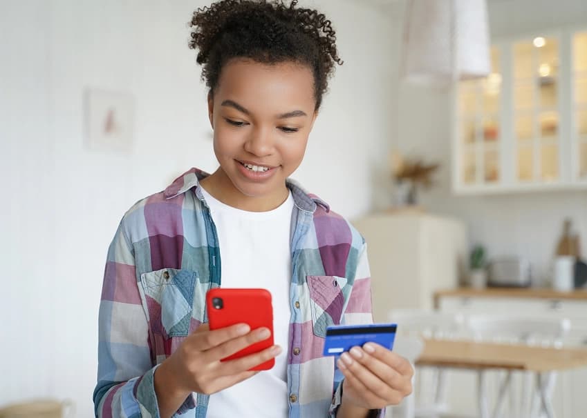 Smiling young person holding a credit card and red smartphone for online banking