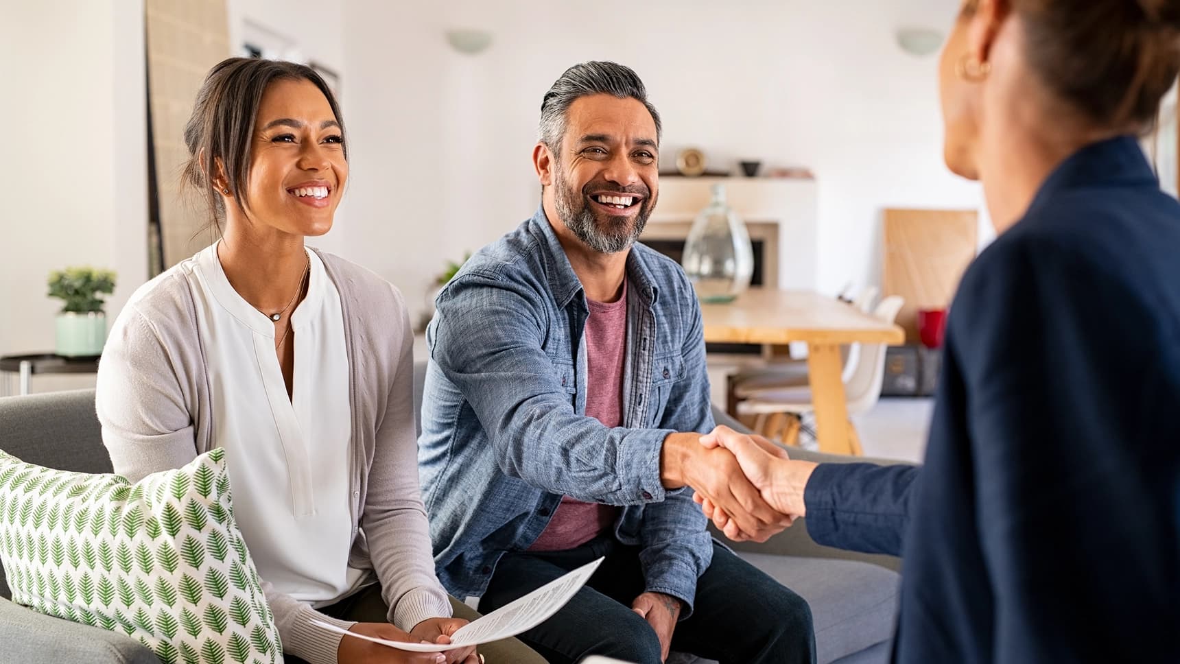 Couple smiling and shaking hands with a mortgage loan advisor during a home consultation