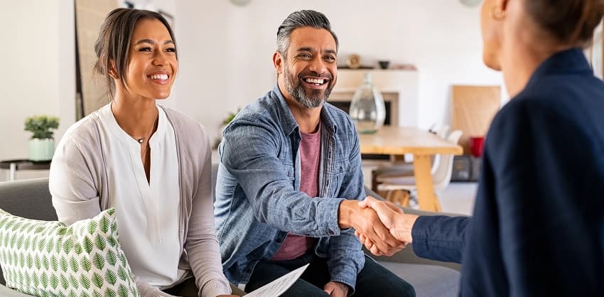 Smiling couple shaking hands with a financial advisor during a home loan or wealth management consultation