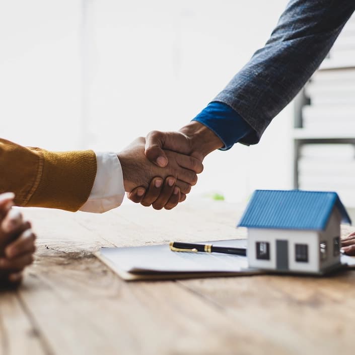 Handshake over a signed mortgage loan agreement with a model house on the table