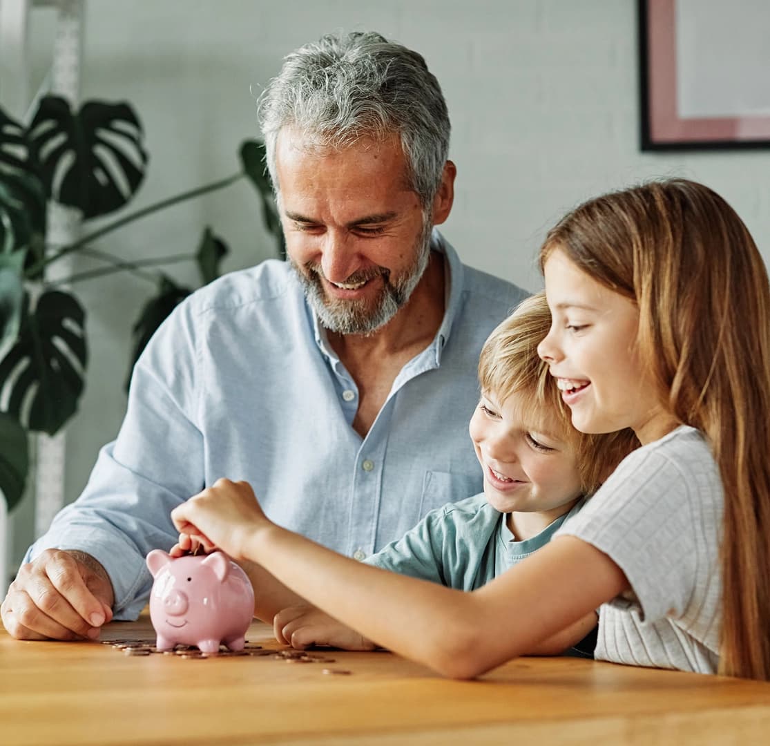 Father and two children smiling while putting coins into a pink piggy bank for savings