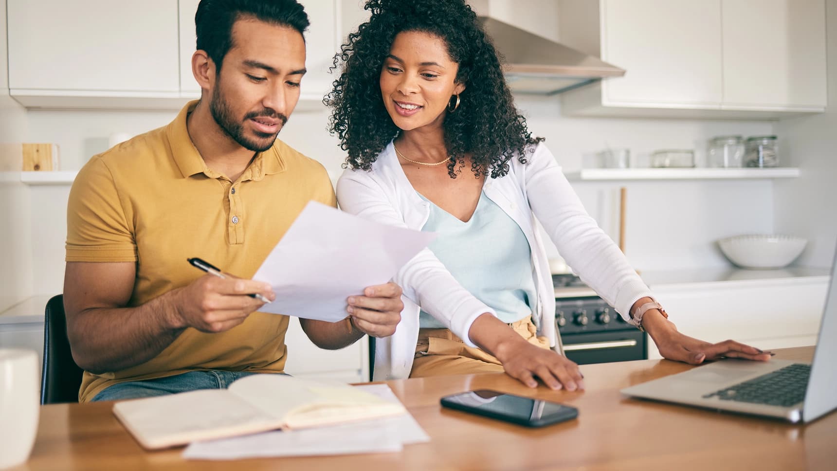 Couple reviewing mortgage loan documents together at a kitchen table with a laptop nearby