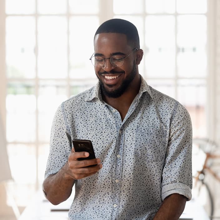 Smiling man with glasses and beard looking at his smartphone