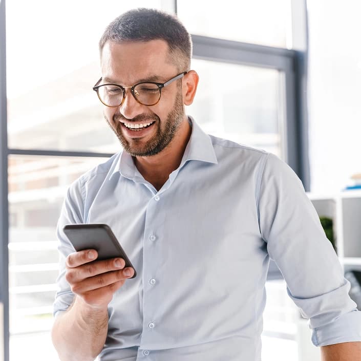 Smiling man in glasses reviewing his online banking on a smartphone in a bright office