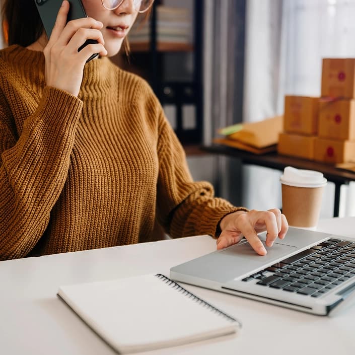 Woman multitasking on a phone call while using a laptop for small business banking
