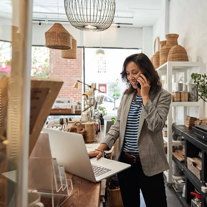 Small business owner on phone while reviewing finances on laptop in her shop