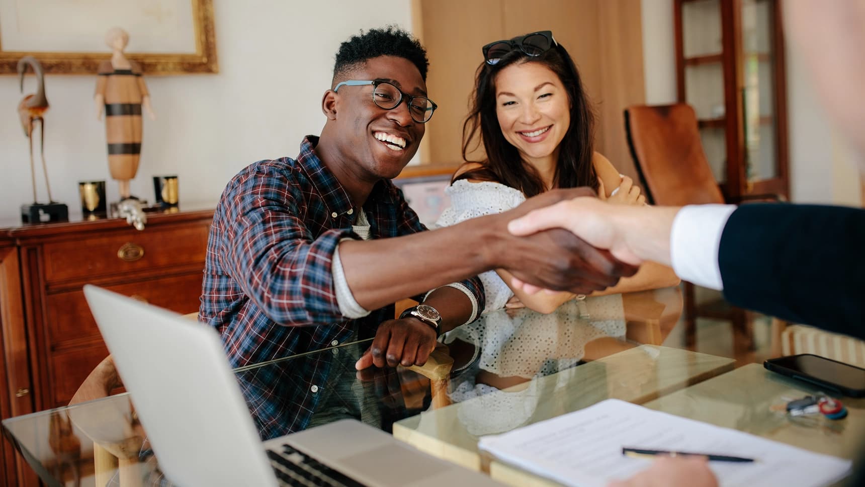 Couple smiling and shaking hands with a banker after securing a mortgage loan