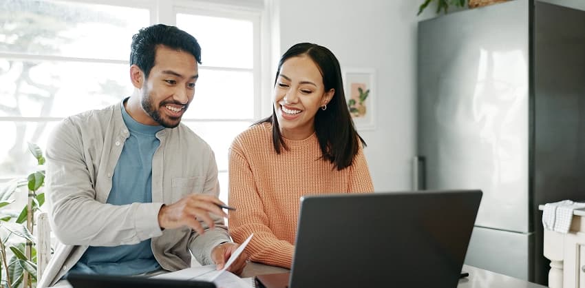 Couple smiling while reviewing home loan or savings account options on a laptop