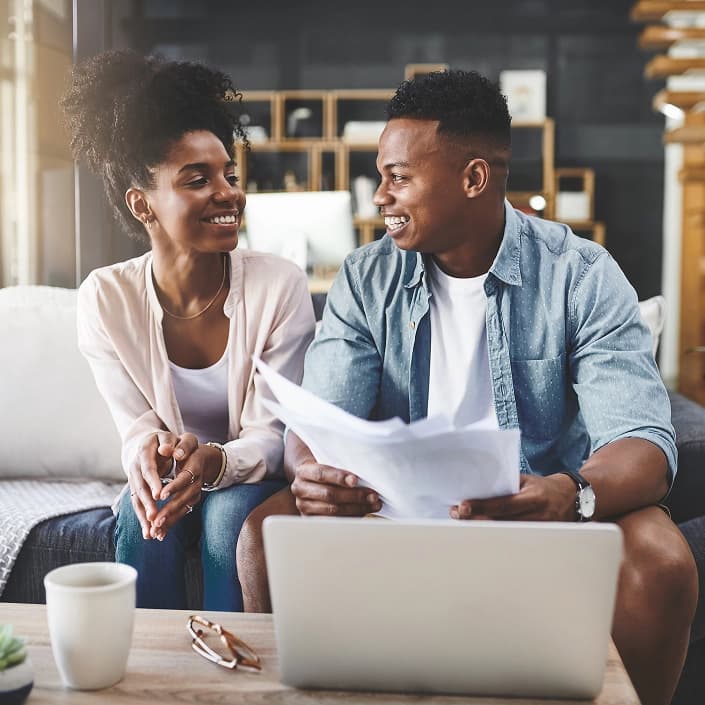 Happy couple reviewing savings account or loan documents together at home with a laptop nearby