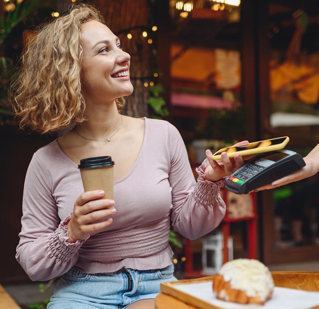 Woman making a contactless mobile payment at a café while holding a coffee cup