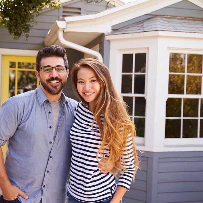 Smiling couple standing in front of their new home after securing a home loan