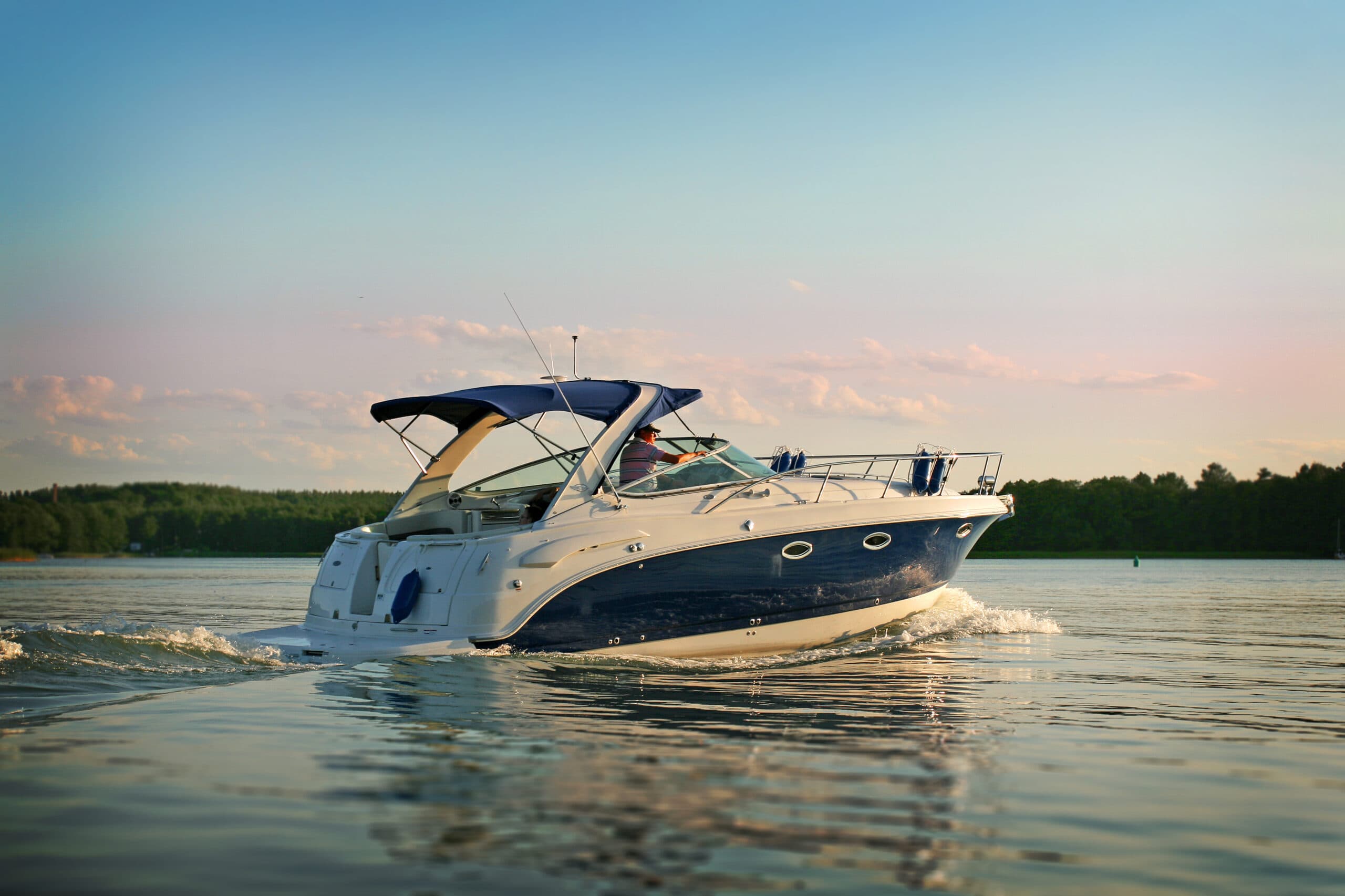 Person driving a motorboat across calm water at sunset