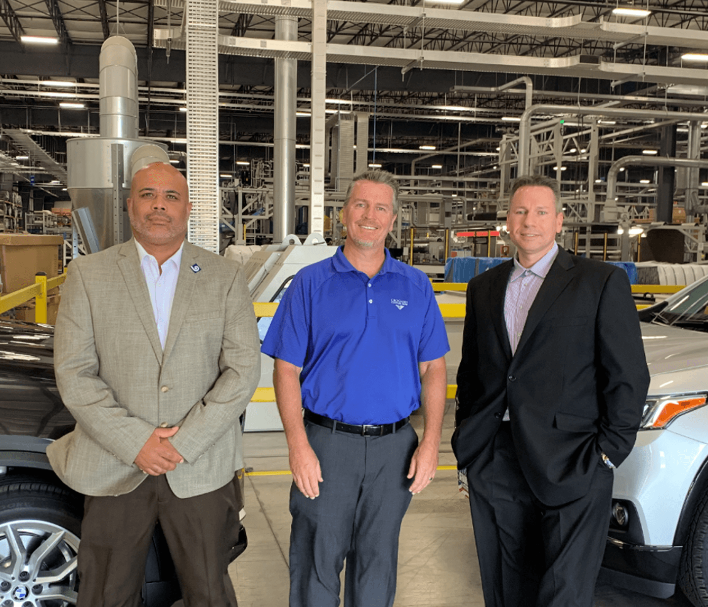 Three men standing inside a large manufacturing facility beside vehicles, representing Croghan Bank business lending