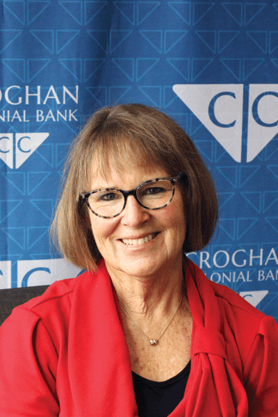 Smiling woman in a red jacket wearing glasses posed in front of a Croghan Colonial Bank backdrop