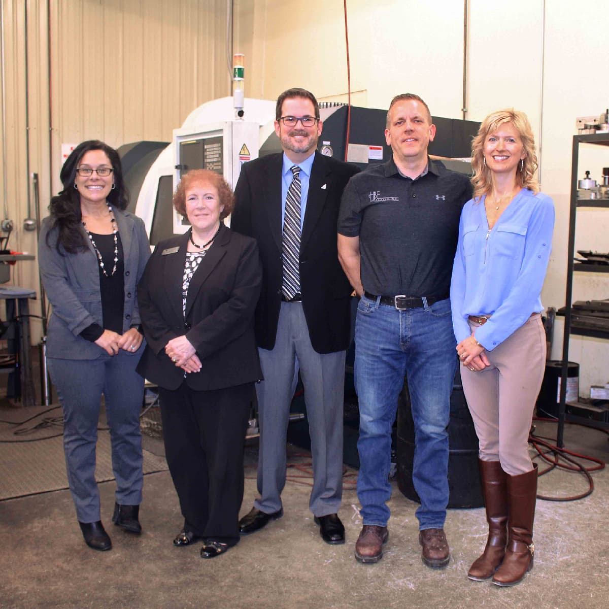 Five people posing together in an industrial facility in front of a CNC machine.